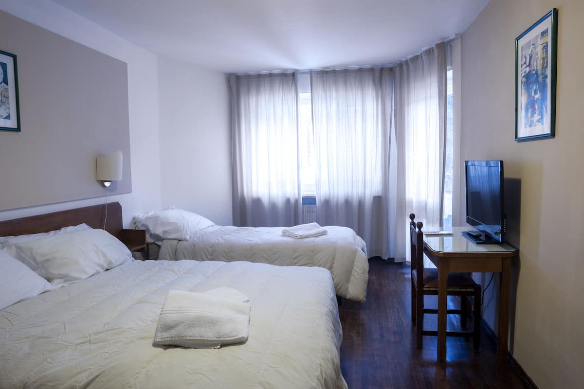 Une chambre d’hôtel avec deux lits, un bureau avec un ordinateur et une télévision.