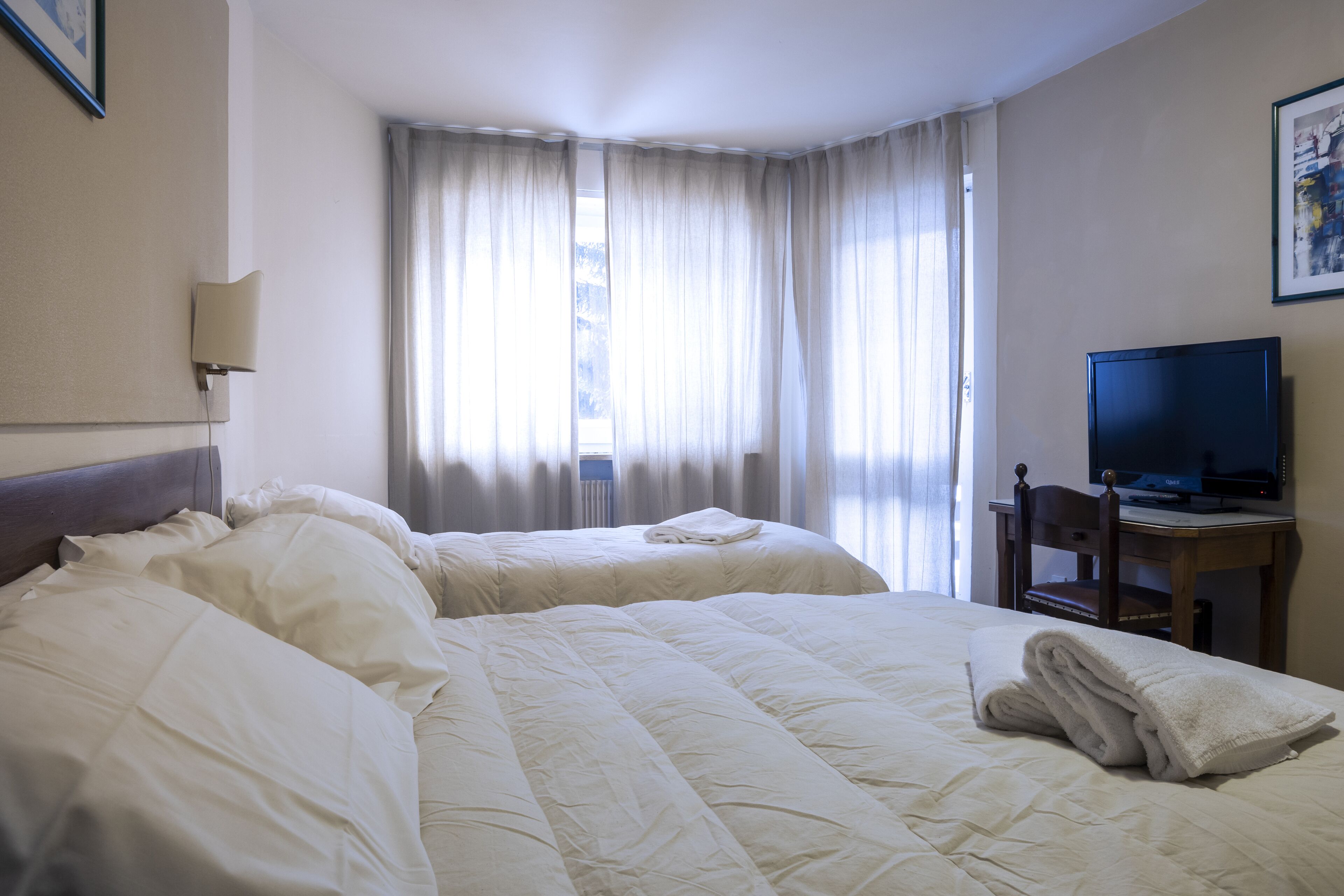 A hotel room with two beds, a television on a wooden table, and a window with curtains.