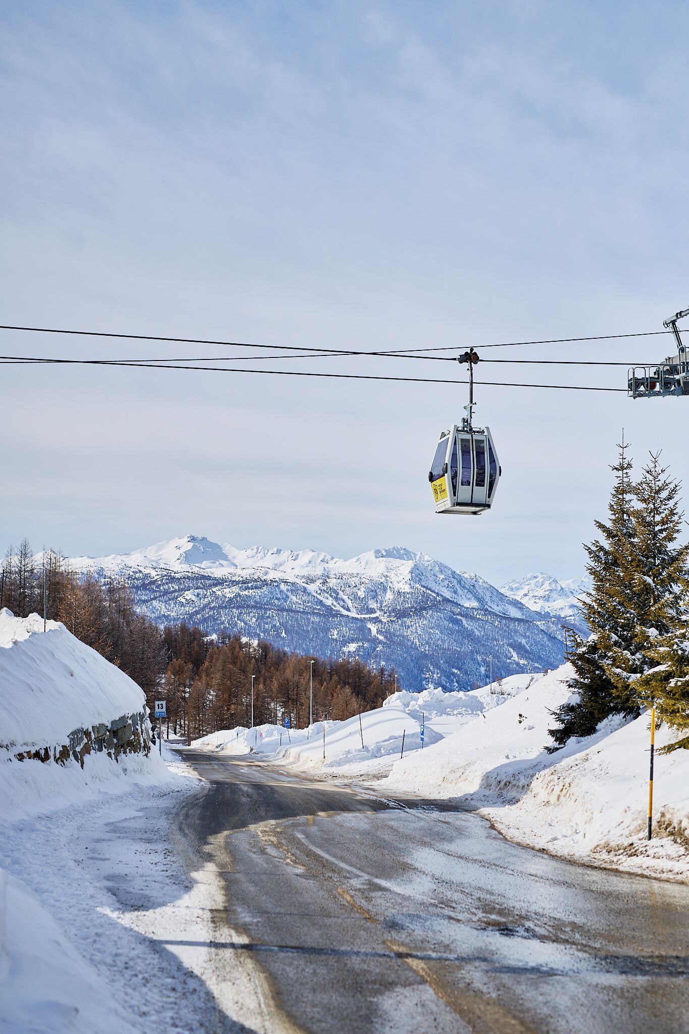 A road with a cable car in the background, snow-covered landscape, and mountains.