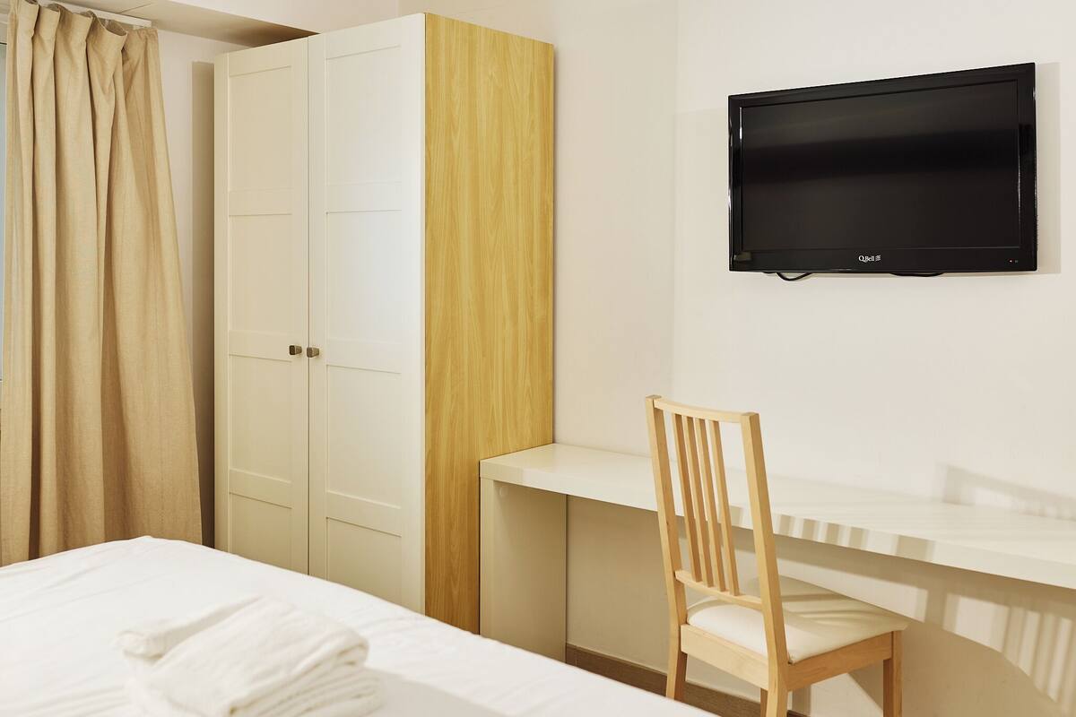 Une chambre d’hôtel équipée d’un lit, d’un bureau, d’une chaise, d’une armoire et d’un téléviseur fixé au mur.