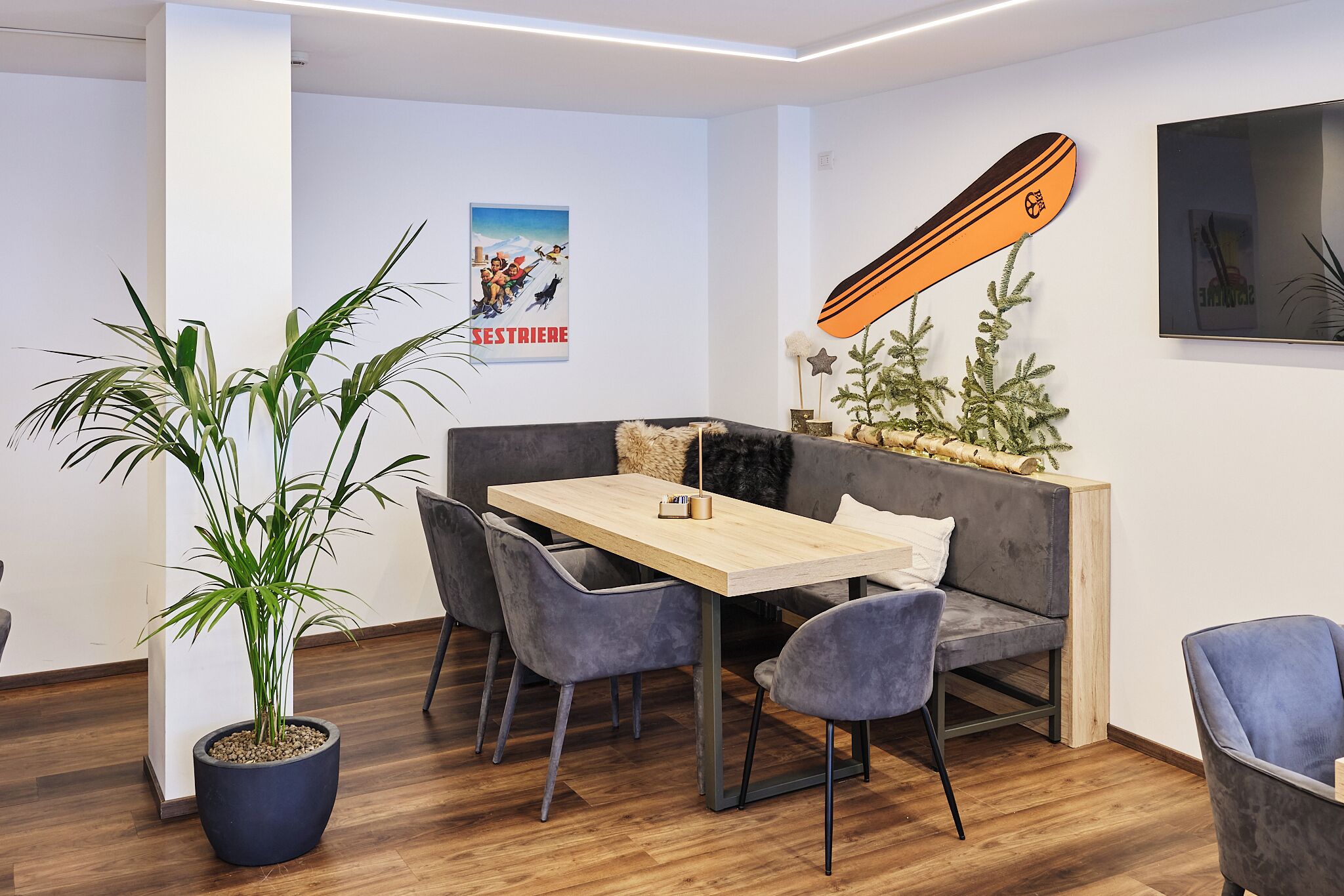 A modern dining area with a wooden table, grey upholstered chairs, a grey sofa, and a potted plant.