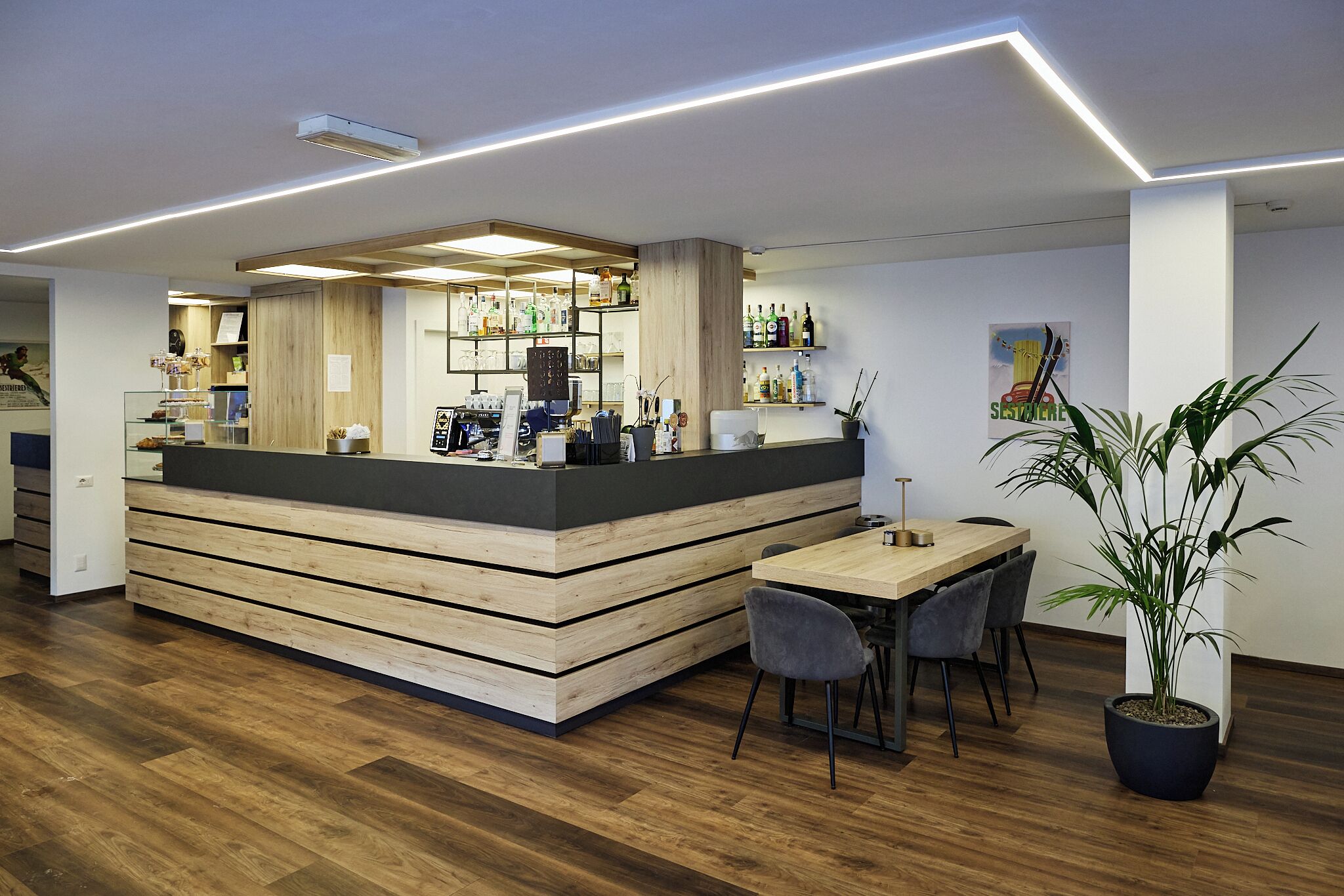 A modern bar area with a wooden counter, seating, and a potted plant.