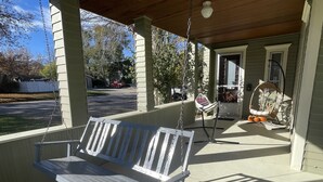 A covered porch with a wooden bench, a wicker chair, and a rocking chair.