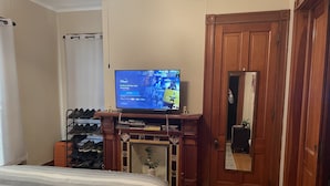 A bedroom with a bed, a TV on a wooden stand, a shoe rack, and a door.