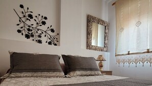 A bedroom with a large bed, a decorative wall piece, a mirror, and a window with curtains.