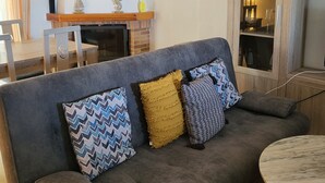 A living room with a grey sofa, patterned cushions, a wooden cabinet, and a fireplace.