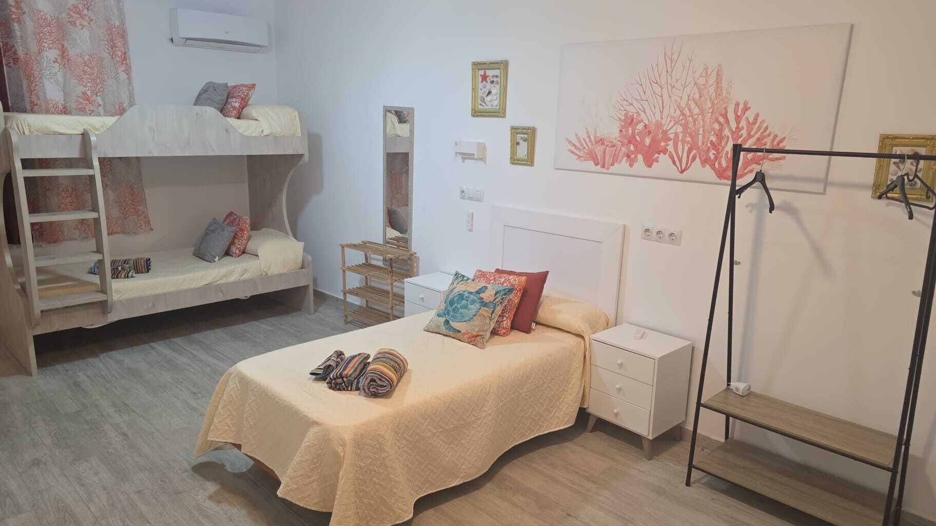 A room with bunk beds, a single bed, a bedside table, a nightstand, a wardrobe, and a wall with artwork.