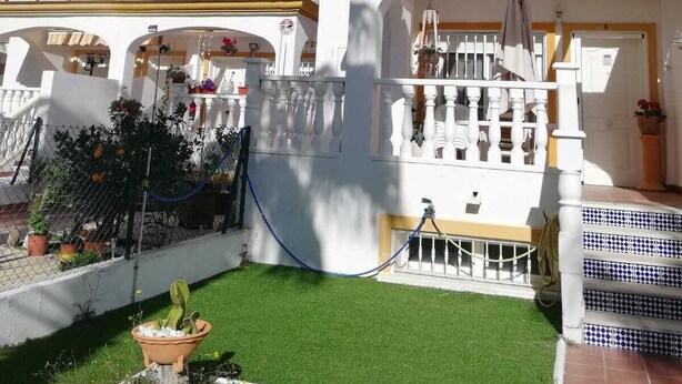 A white building with balconies, a small garden with artificial grass, and a blue hose.