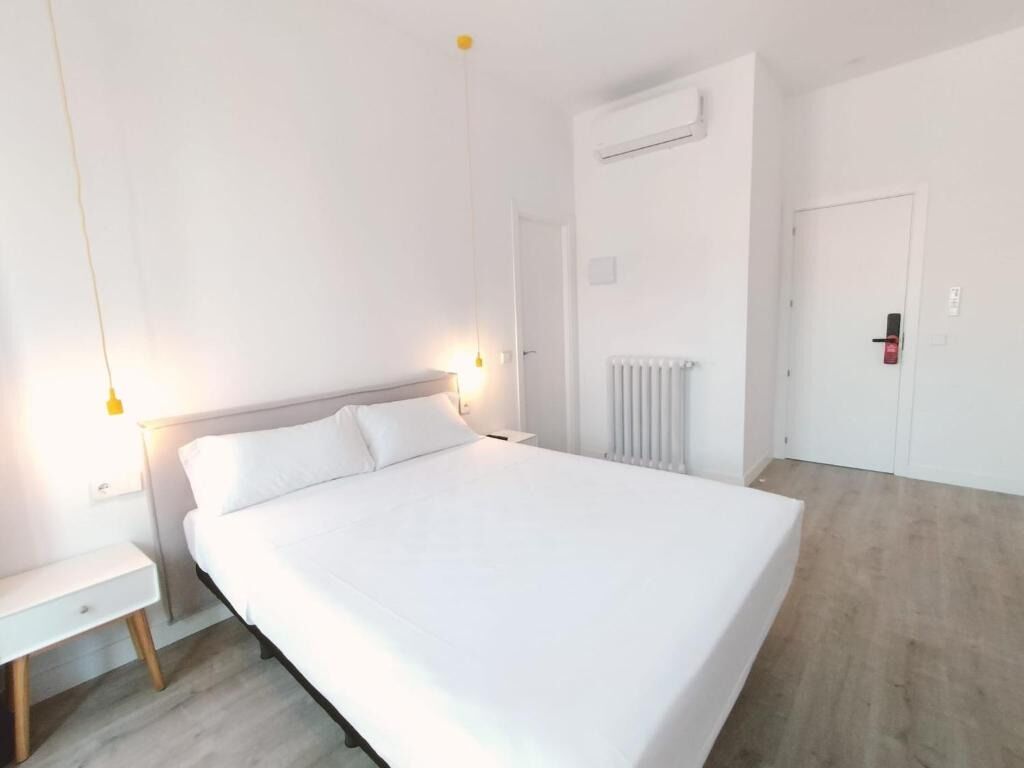 A bedroom with a large bed, a bedside table, a hanging light, and a radiator.