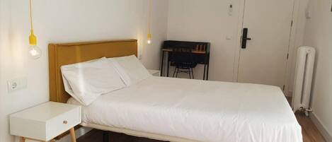 A single bed with a wooden headboard, a bedside table, a chair, and a desk with a chair.