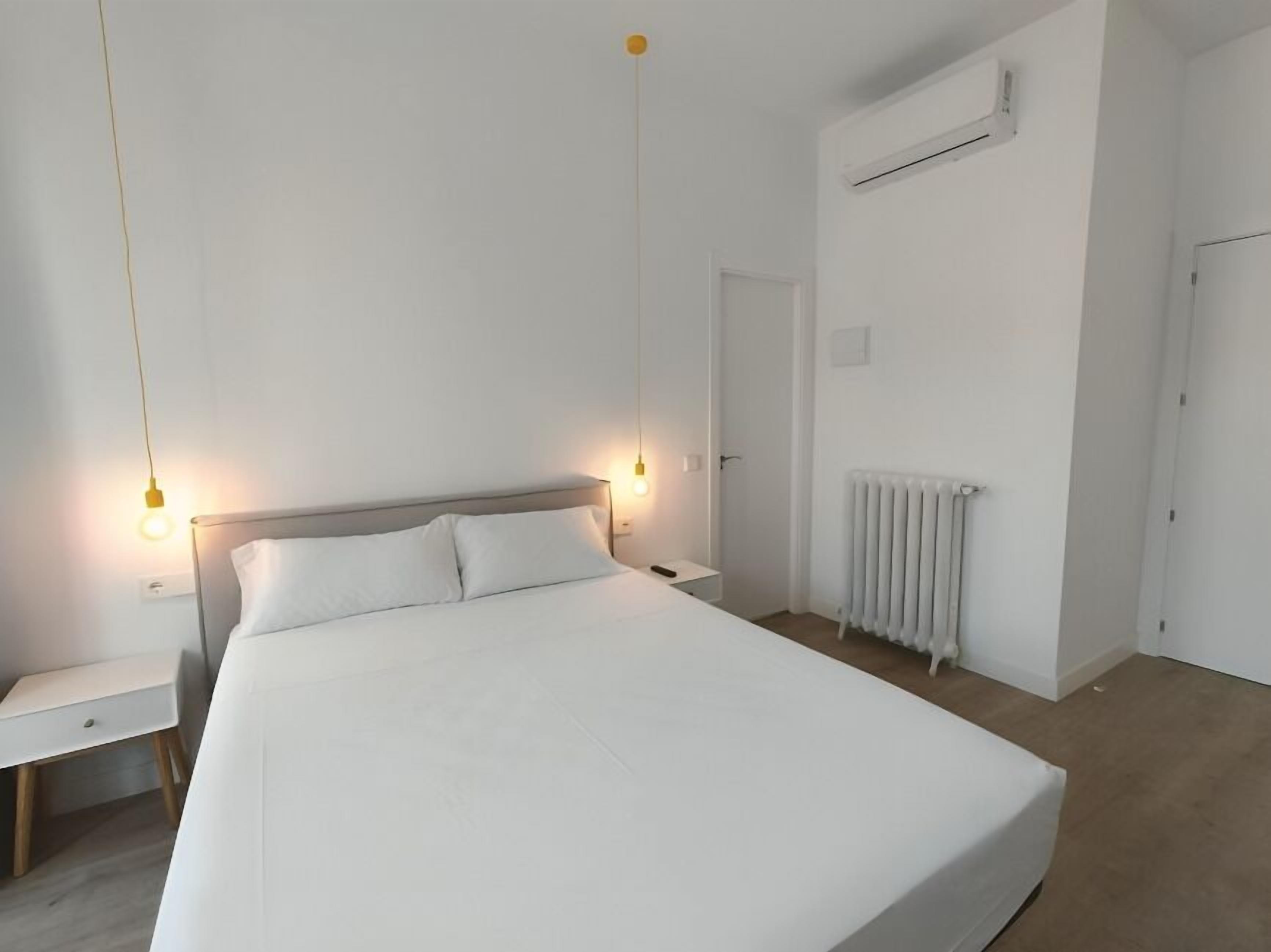A minimalist bedroom with a large bed, bedside tables, a radiator, and an air conditioning unit.