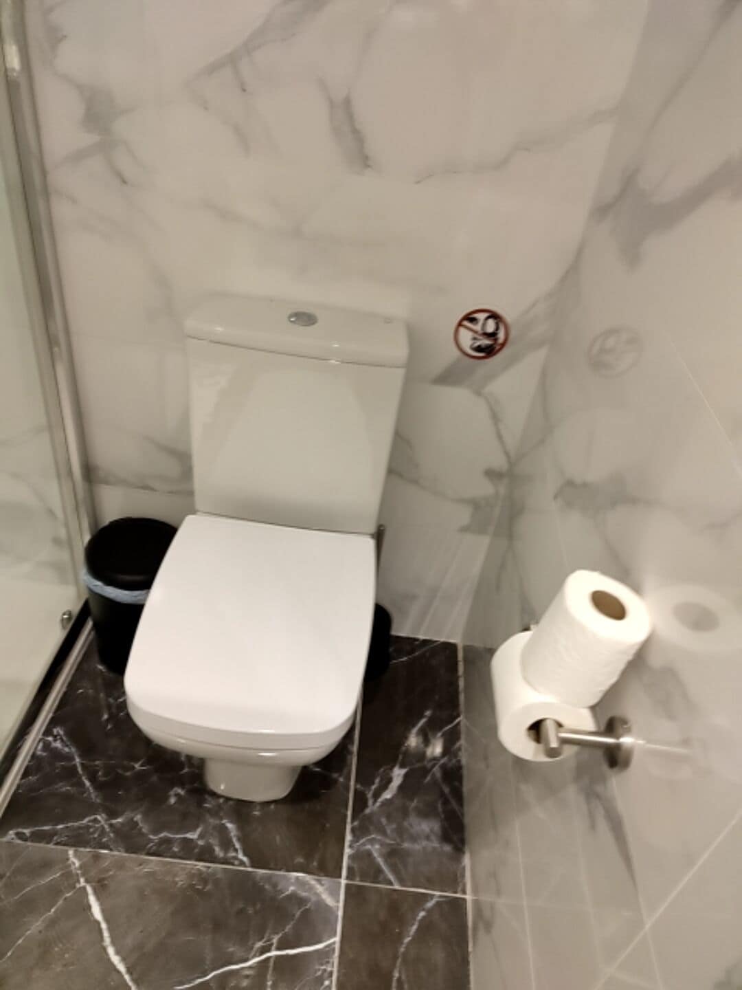 Ein Badezimmer mit Toilette, Mülleimer und Toilettenpapierhalter.