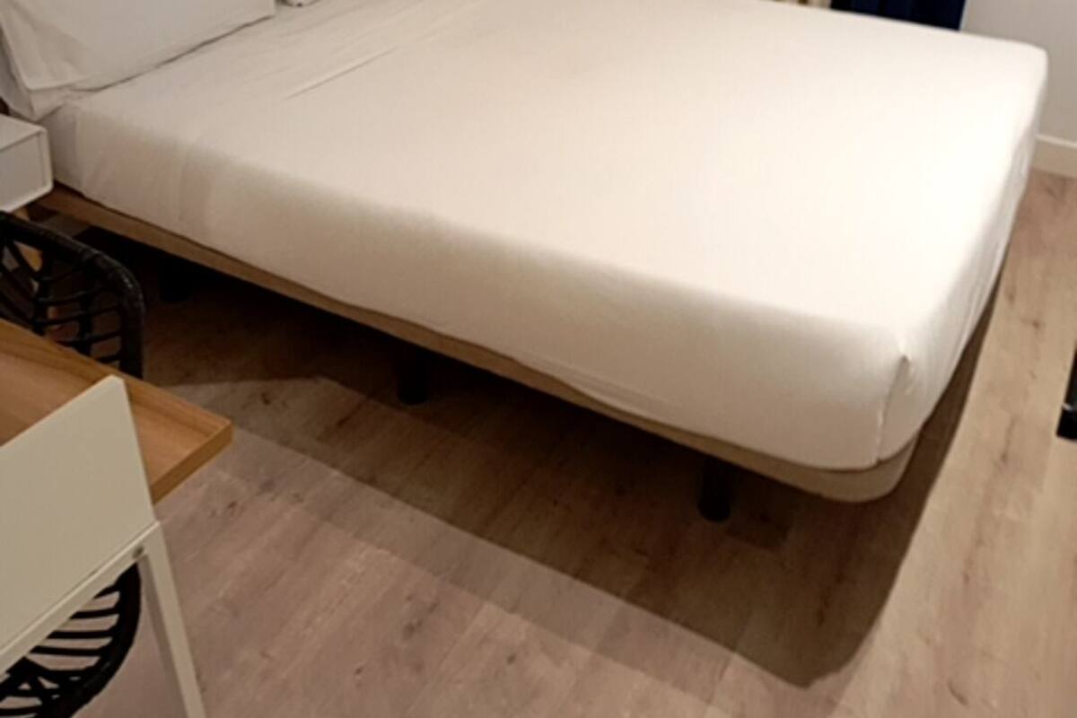 Een eenpersoonskamer met houten vloer, nachtkastje, stoel en radiator.