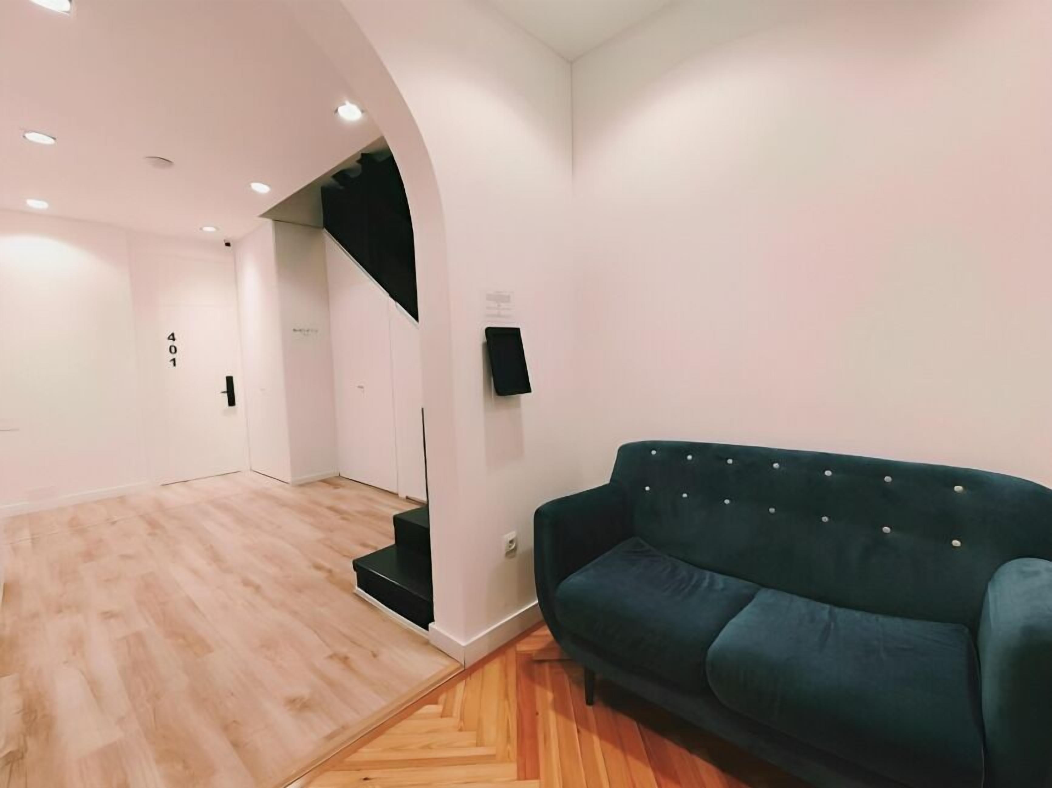 A spacious room with a wooden floor, a dark green sofa, and a black wall-mounted speaker.