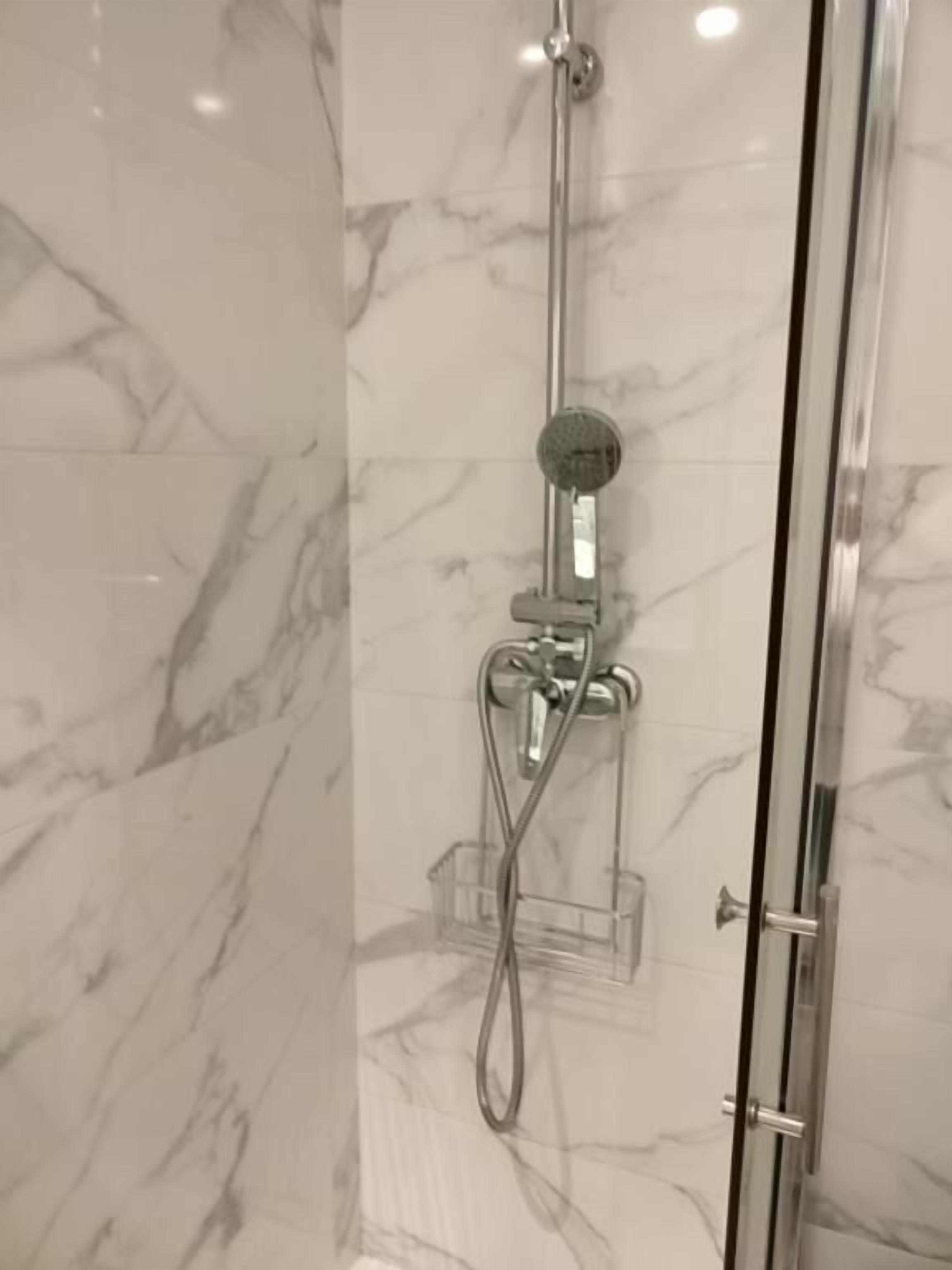 A glass-enclosed shower with a handheld showerhead and a wall-mounted faucet.