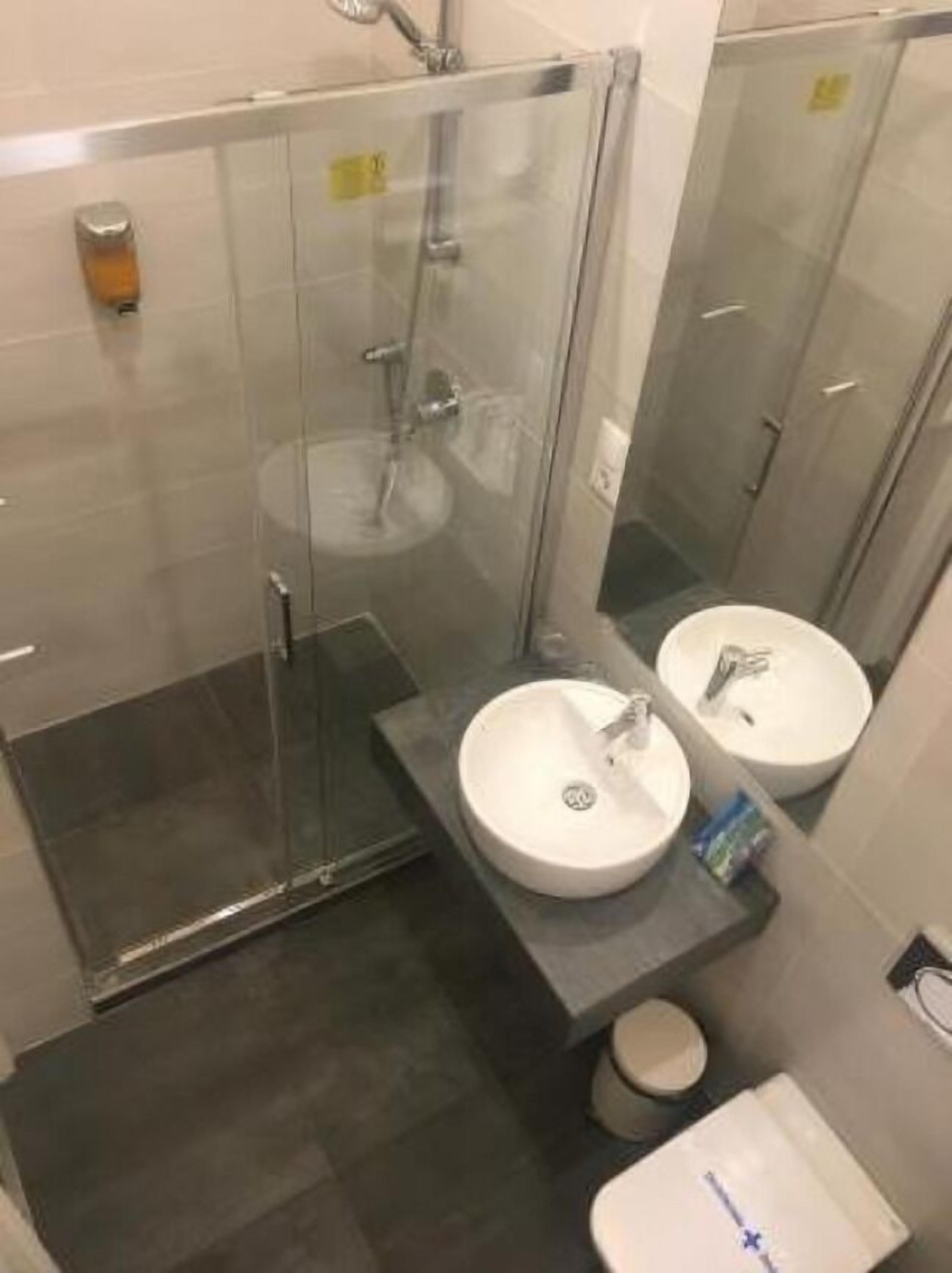 A modern bathroom with a glass-enclosed shower, two sinks, and a toilet.