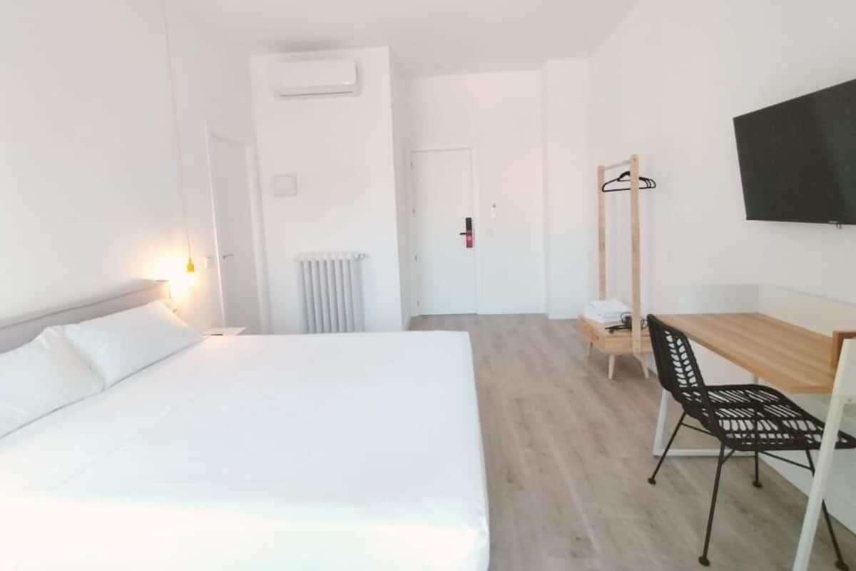 Een hotelkamer met een bed, een bureau, een stoel, een televisie en een kapstok.