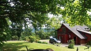 Une grange rouge avec une voiture garée devant, entourée d’une cour verdoyante et d’arbres.