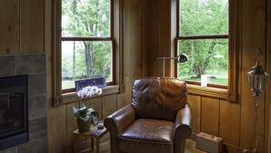Une pièce chaleureuse avec un fauteuil en cuir, une petite table sur laquelle est posé un vase de fleurs et une cheminée.