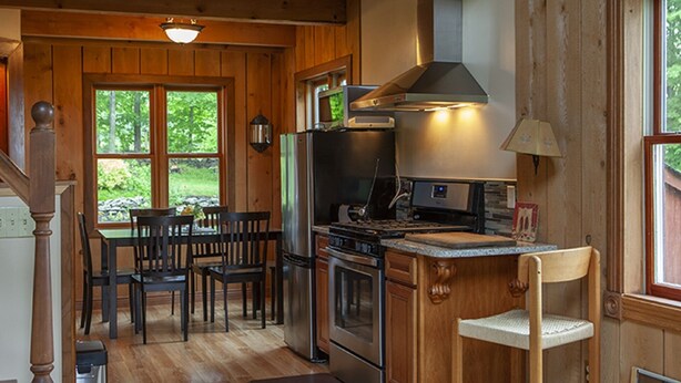 Une cuisine rustique aménagée dans une cabane en bois, avec un coin repas, de grandes fenêtres et un poêle.