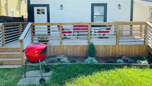 Une terrasse avec un barbecue, un petit arbre et une clôture en bois.