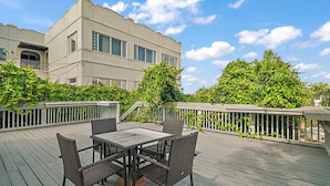 A deck with a table and chairs, surrounded by greenery and a building in the background.