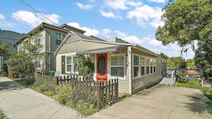 A single-story house with a red door, a small porch, and a picket fence.