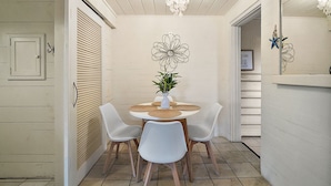 A dining area with a round table, four white chairs, a potted plant, and a decorative wall piece.