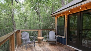A wooden deck with Adirondack chairs and a small table, surrounded by a forest. - Secret Stash: Secluded Treehouse Overlooking Creek (Dahlonega)