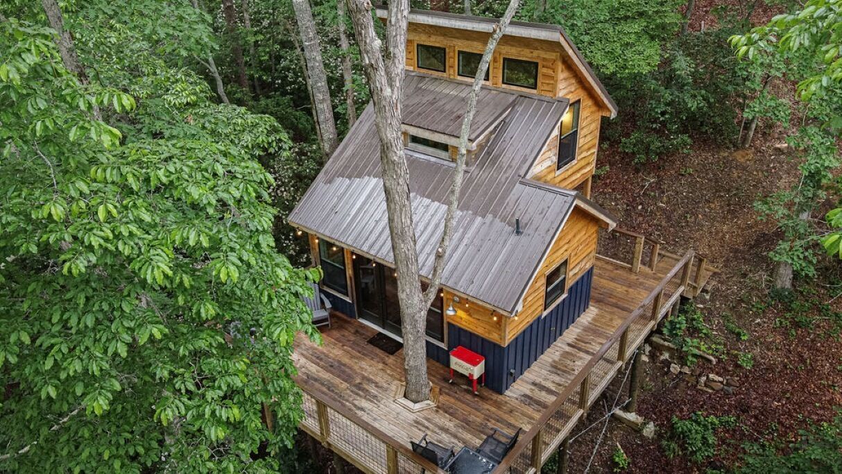 A wooden cabin with a deck, surrounded by dense forest.
