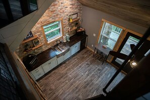 A kitchen with a stone wall, wooden ceiling, and large windows. - Secret Stash: Secluded Treehouse Overlooking Creek (Dahlonega)