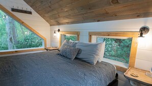 A bedroom with a large bed, two bedside tables, and a window with a view of trees. - Secret Stash: Secluded Treehouse Overlooking Creek (Dahlonega)