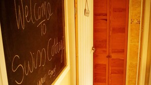 A hallway with a chalkboard displaying "Welcome to Swiss Cottage" and a door leading to a room. - Idyllic 2 bedroom Canal facing Cottage in Hopwas (Hopwas)
