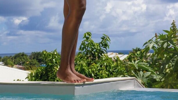Eine Person in einem roten Badeanzug steht am Poolrand, im Hintergrund ein klarer Himmel mit Wolken.
