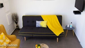 Ein modernes Wohnzimmer mit einem dunklen Sofa, einer gelben Decke und einem kleinen runden Tisch mit einer Flasche.