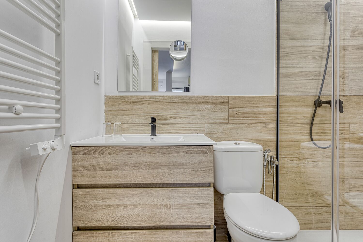 A modern bathroom with a wooden vanity, a white toilet, and a glass shower enclosure.