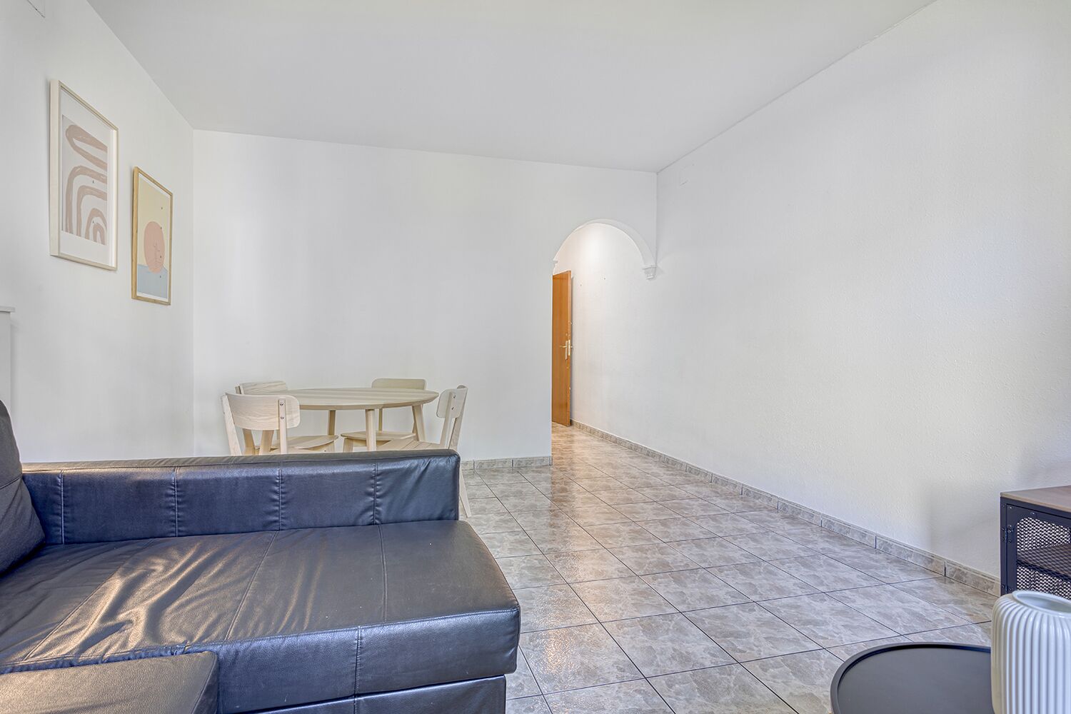 A spacious living area with a leather sofa, a wooden dining table, and chairs.