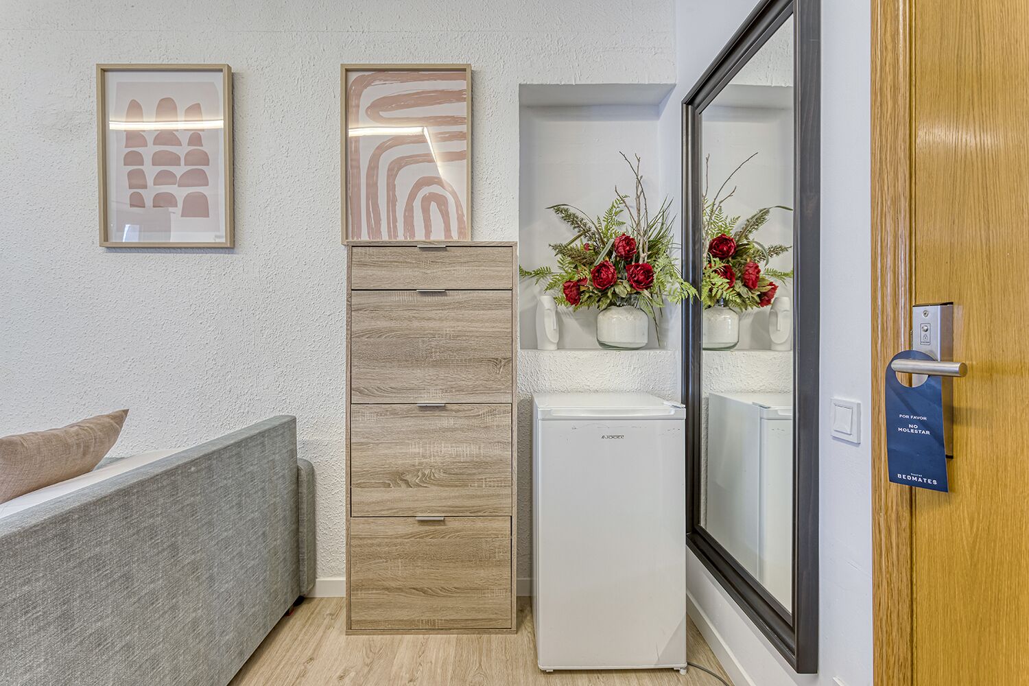 A hotel room with a bed, a wooden cabinet, a refrigerator, and a mirror.