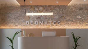 A reception desk with a stone wall backdrop, a modern light fixture, and two potted plants. - Hostal Bedmates (Barcelona)