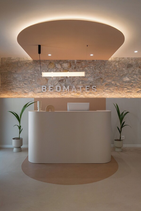 A reception desk with a stone wall backdrop, a modern light fixture, and two potted plants.