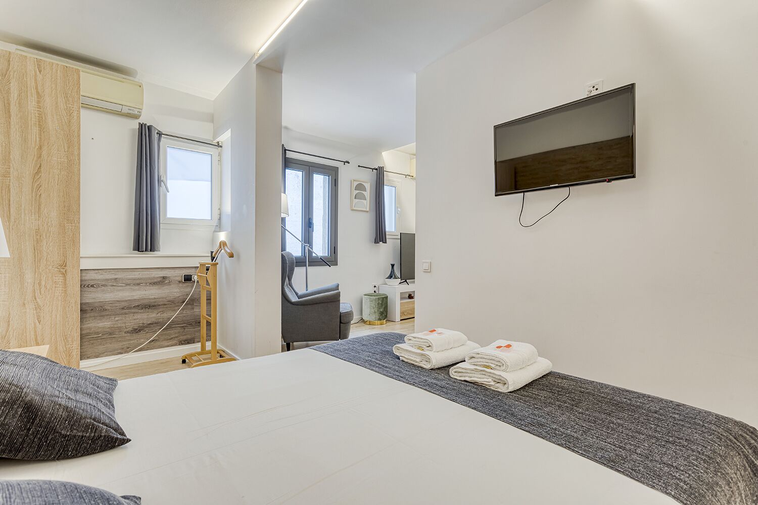 Una habitación de hotel moderna con una cama, un televisor montado en la pared y una ventana con cortinas.