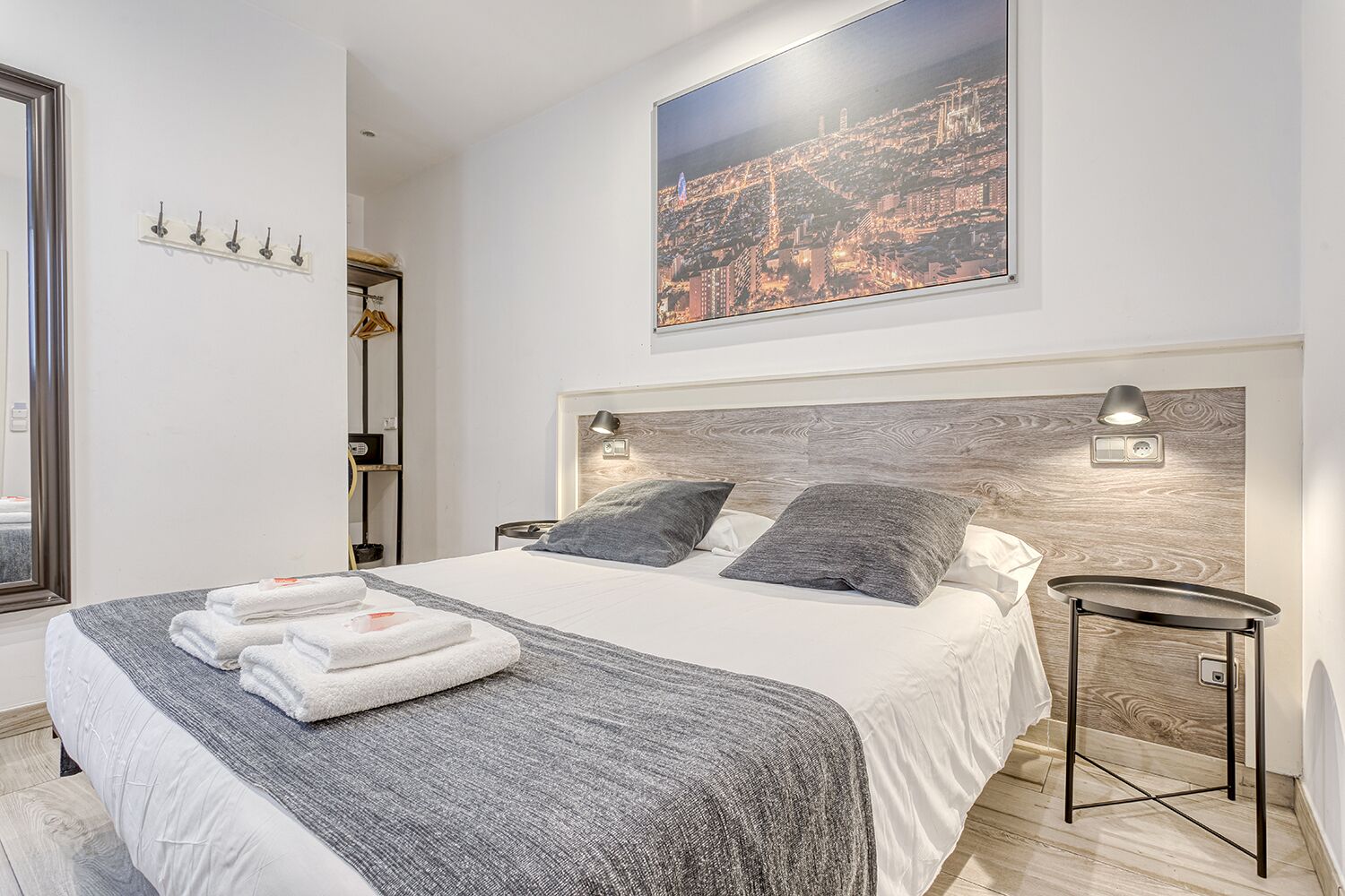 Een moderne slaapkamer met een groot bed, twee bedlampen, uitzicht op een stadsbeeld, een kapstok en een kleine tafel.