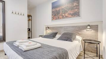 Een moderne slaapkamer met een groot bed, twee bedlampen, uitzicht op een stadsbeeld, een kapstok en een kleine tafel.