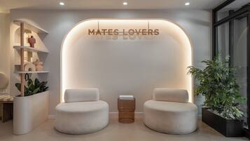 A modern interior with two cushioned seating areas, a wall-mounted sign reading 'MATES LOVERS,' and a potted plant.