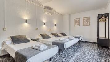 Habitación de hotel con cuatro camas, cada una con almohada y toalla. Luces y cuadros decoran las paredes.