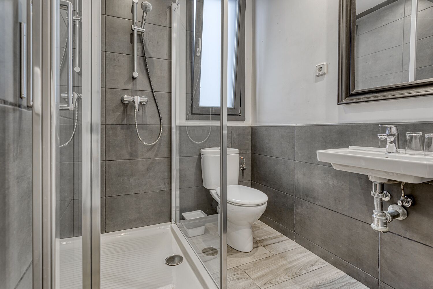 Un baño moderno con cabina de ducha de vidrio, inodoro y lavamanos con espejo arriba.