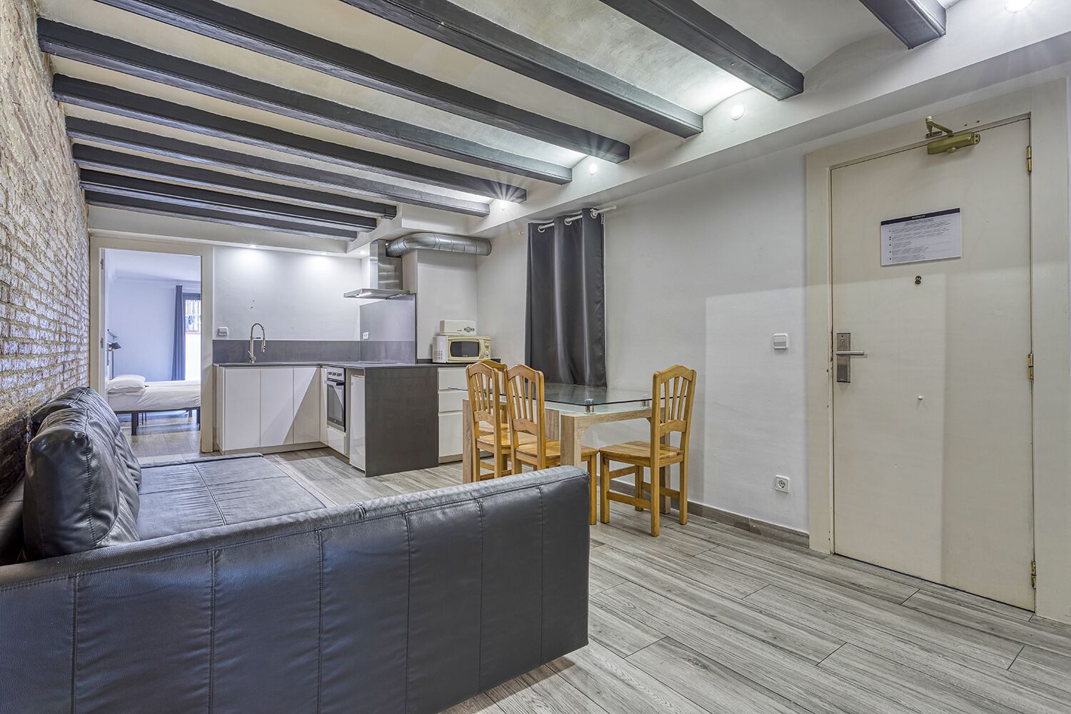 A compact living space with a kitchenette, a dining area with two wooden chairs, a sofa, and a door with a sign.