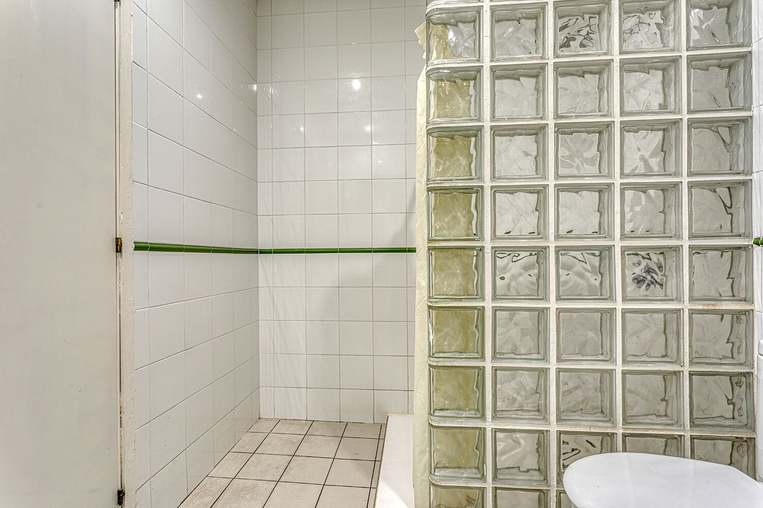 A bathroom with white tiled walls, a glass shower enclosure, and a white toilet.