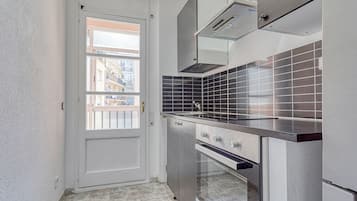 Ett kompakt kök med en inbyggd ugn, en spishäll och ett fönster med utsikt över ett bostadsområde.