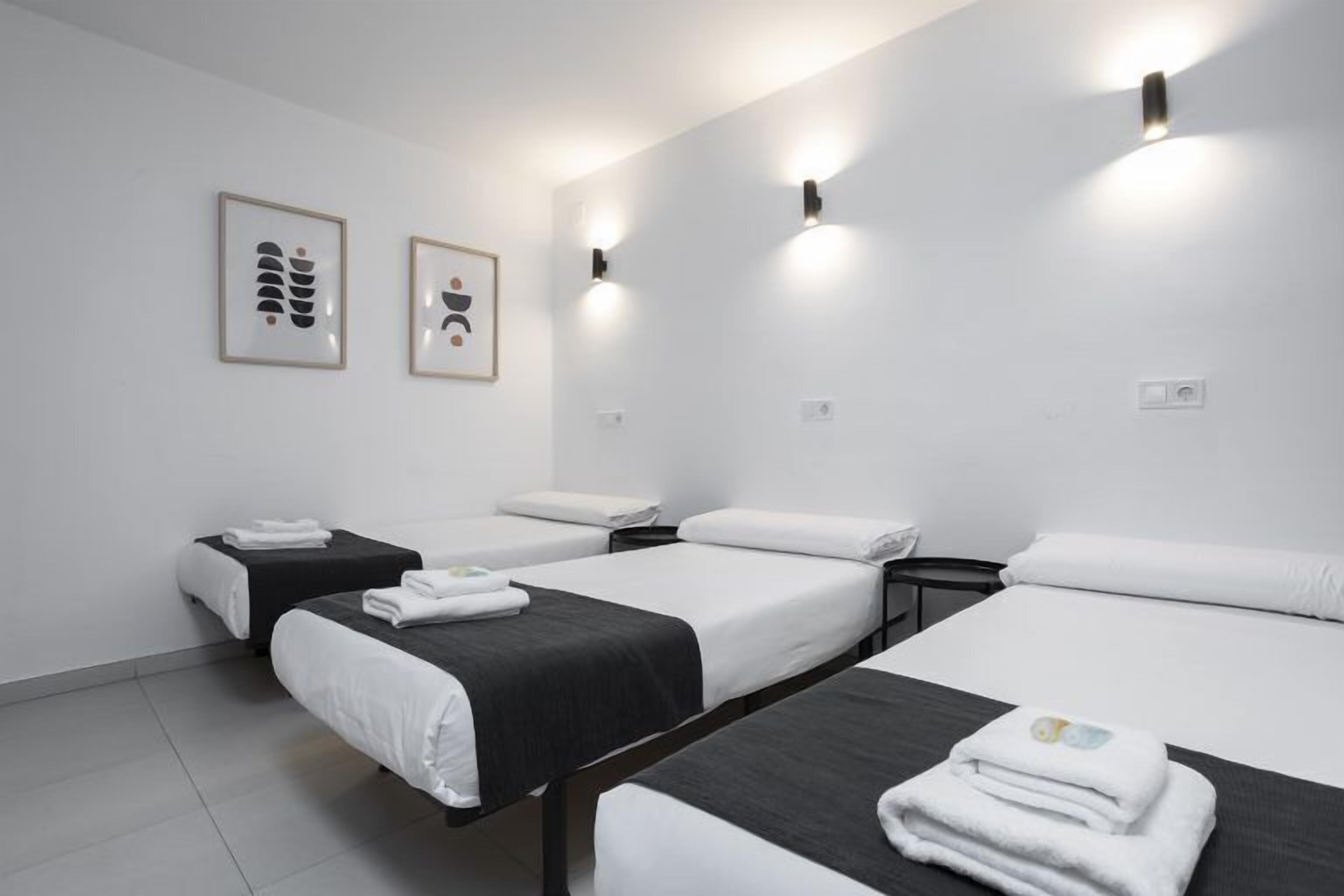 A hotel room with four beds arranged in a U-shape, white bedding, and two framed artworks on the wall.